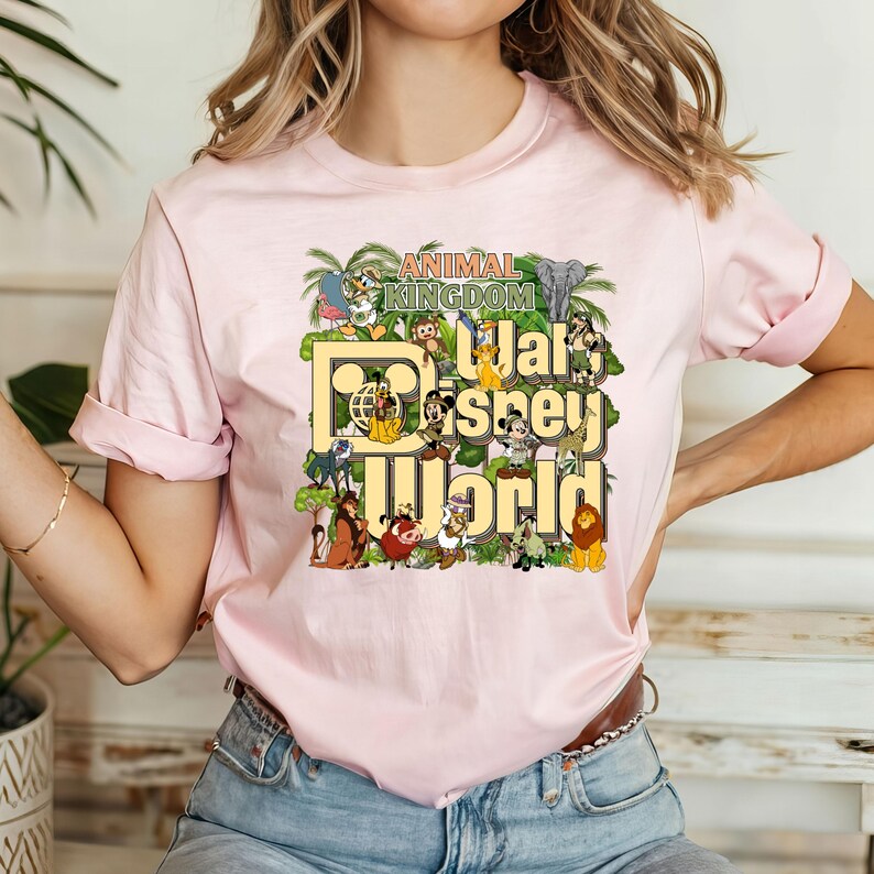 Pu&ograve; includere: Maglietta rosa con una grafica di vari personaggi Disney di Animal Kingdom, tra cui Topolino, Paperino, Pippo e Simba. Il testo "Animal Kingdom" e "Walt Disney World" &egrave; stampato sulla maglietta.