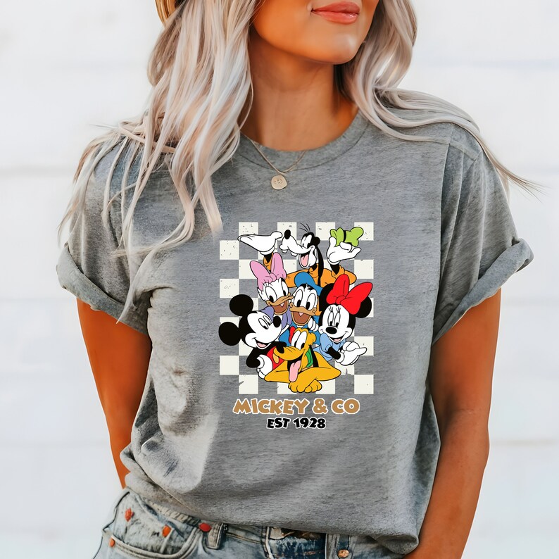 Puede incluir: Camiseta gris con un fondo a cuadros con Mickey Mouse y sus amigos. El texto "Mickey & Co. Est 1928" est&aacute; impreso debajo de la imagen.