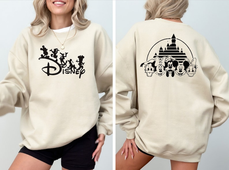 Puede incluir: Una sudadera beige con un logotipo de Disney negro y personajes en la parte delantera y una silueta negra del castillo de Disney y personajes en la parte posterior.