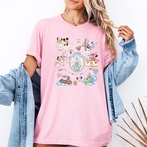 May include: Pink t-shirt featuring a colorful graphic with various Disney characters and the text "Best Day Ever" in a decorative frame. The design includes Mickey and Minnie Mouse, a castle, and other themed elements.