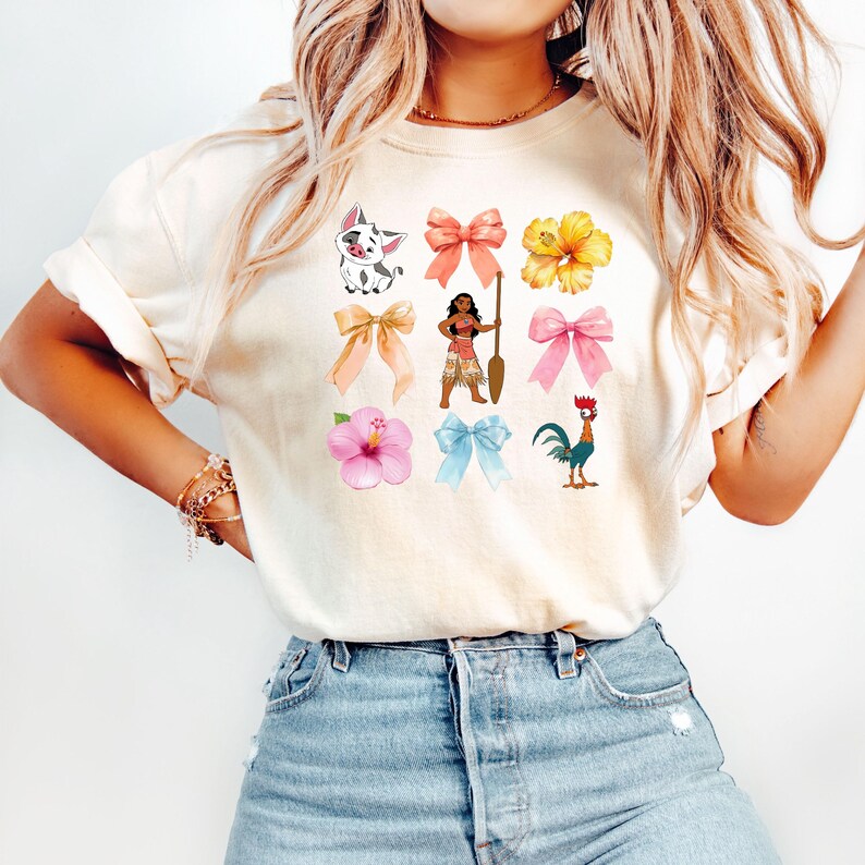 Pu&ograve; includere: Una maglietta bianca con un design colorato che presenta un maiale, una donna con una pagaia, un gallo, fiori e fiocchi.