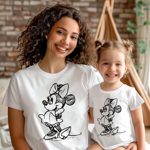 May include: A white t-shirt with a black and white sketch of Minnie Mouse on the front. A matching t-shirt is worn by a young girl.