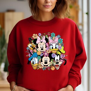 May include: Red sweatshirt with a colorful graphic print of Mickey Mouse, Minnie Mouse, Donald Duck, Goofy, and Pluto surrounded by flowers.