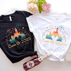 May include: Two t-shirts with a retro rainbow design of Cinderella's castle and the text "Class of 2025". One shirt is black and the other is white.