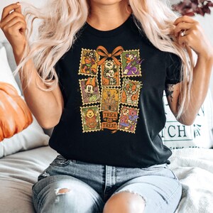 May include: Black t-shirt featuring a collage of Halloween-themed postage stamps with Disney characters. The stamps include images of Mickey Mouse, Donald Duck, and Winnie the Pooh. The words "Trick or Treat" are printed on one of the stamps.