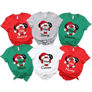 K&ouml;nnte beinhalten: Eine Auswahl an kurz&auml;rmeligen T-Shirts in Rot, Grau, Gr&uuml;n und Wei&szlig;. Jedes Shirt zeigt eine Disney-Grafik mit Weihnachtsm&uuml;tze, Mickey Mouse Ohren und dem Jahr 2024. Auf den Shirts steht "Grandpa", "Daddy", "Grandma", "Sister", "Custom" und "Mommy".