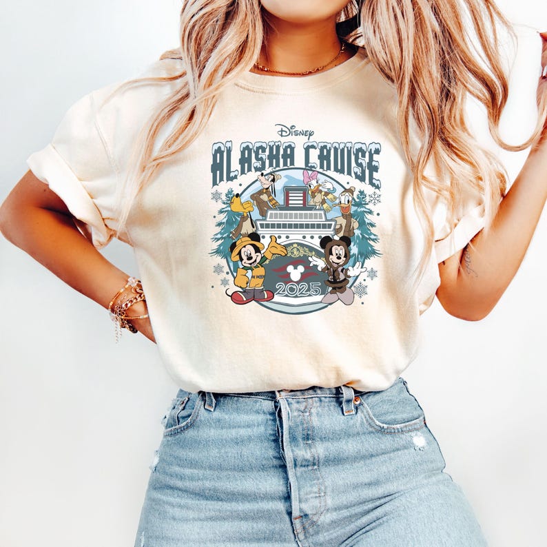 Pu&ograve; includere: T-shirt color crema con un design Disney Alaska Cruise. La grafica include Topolino, Minnie, Paperino e Pippo su una nave da crociera, con la scritta "Alaska Cruise 2025". Il design &egrave; circondato da fiocchi di neve e pini.