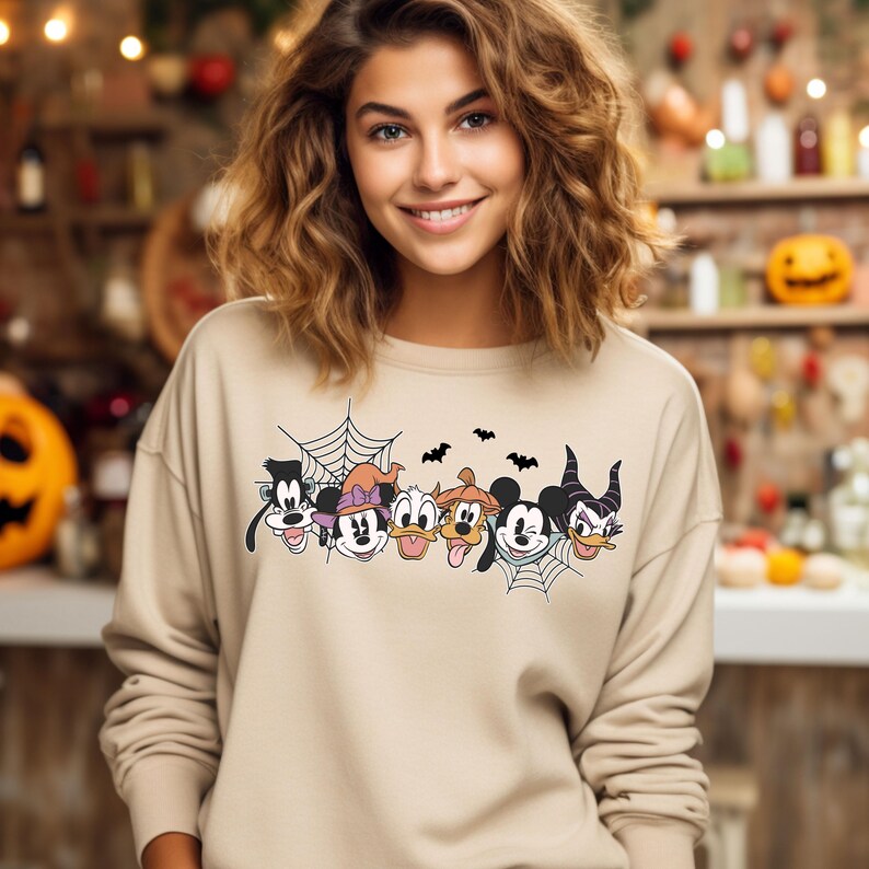 Puede incluir: Una sudadera de color beige con un gr&aacute;fico de Mickey Mouse, Minnie Mouse, Donald Duck, Goofy, Pluto y Mal&eacute;fica en un tema de Halloween. Los personajes est&aacute;n rodeados por una telara&ntilde;a y murci&eacute;lagos.