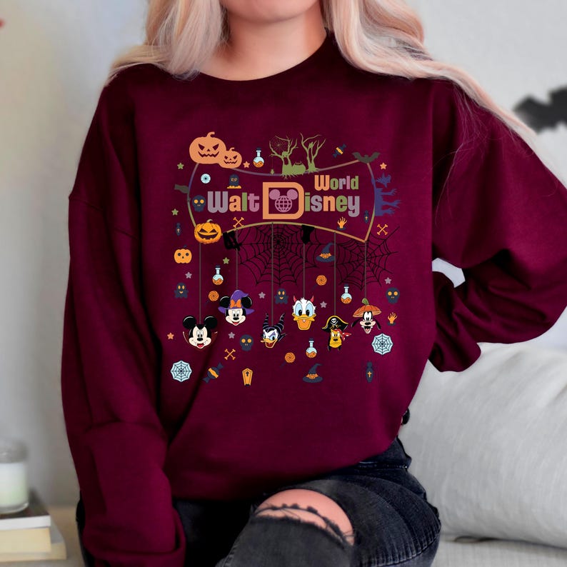 May include: A maroon sweatshirt with a Halloween-themed design featuring Mickey Mouse, Donald Duck, Goofy, and other Disney characters. The design includes the text "Walt Disney World" and various Halloween icons like pumpkins, bats, and ghosts.
