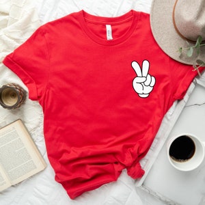May include: Red short-sleeved t-shirt with a white peace sign graphic.