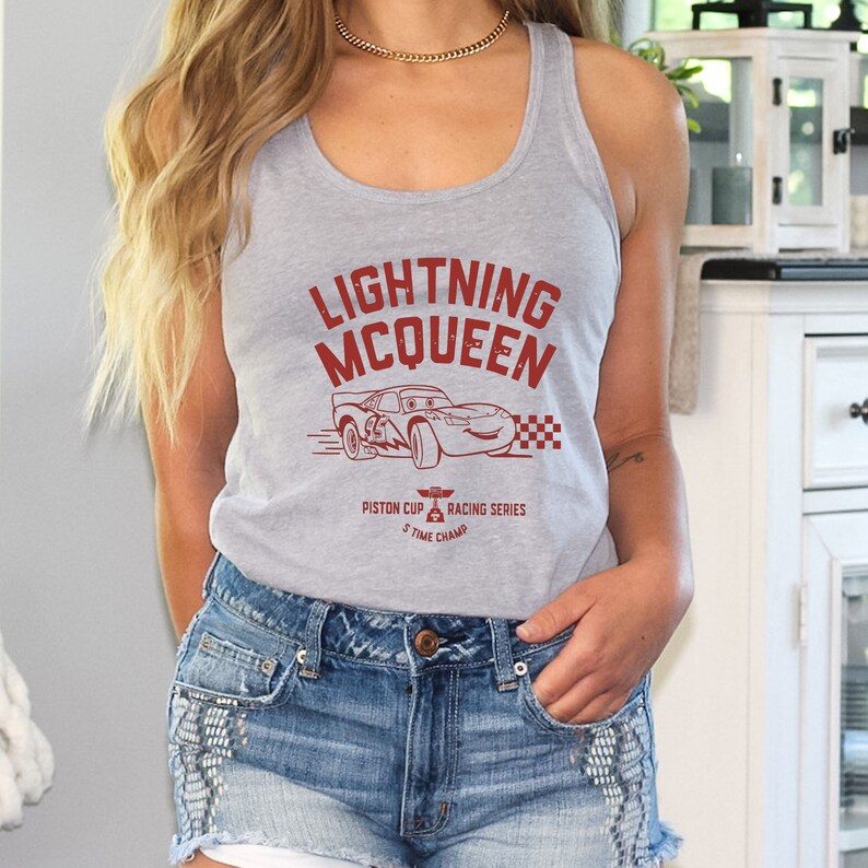 May include: Gray tank top with a red graphic of Lightning McQueen from the Disney Pixar movie Cars. The graphic includes the text "Lightning McQueen", "Piston Cup", and "Racing Series".