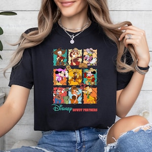 May include: Black t-shirt featuring a colorful graphic of Disney characters in cowboy attire. The design includes Donald Duck, Mickey Mouse, and other characters in a grid pattern. The text "Disney Howdy Partners" is printed below the grid.