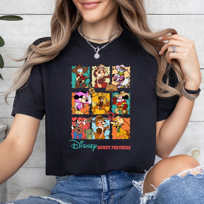 May include: Black t-shirt featuring a colorful graphic of Disney characters in cowboy attire. The design includes Donald Duck, Mickey Mouse, and other characters in a grid pattern. The text "Disney Howdy Partners" is printed below the grid.