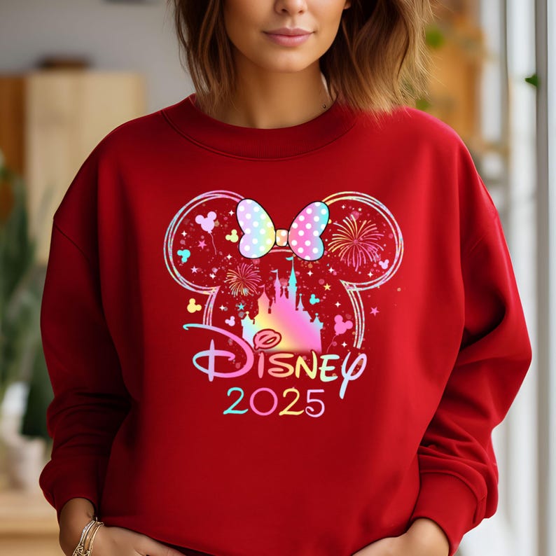 May include: Red sweatshirt with a colorful graphic of Mickey Mouse ears, a bow, and Cinderella's castle. The text "DISNEY 2025" is below the graphic.