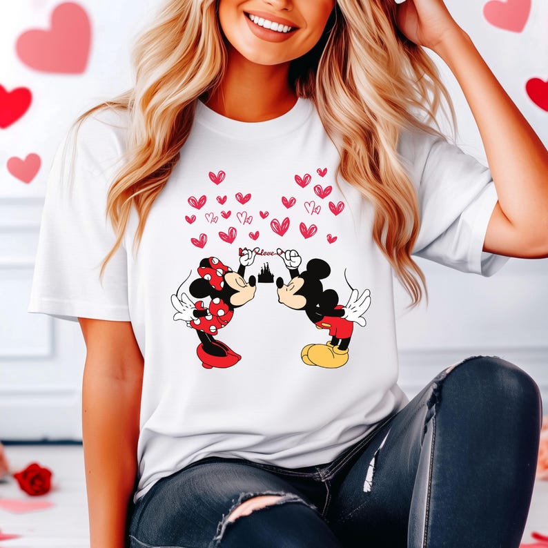 Puede incluir: Camiseta blanca con un gr&aacute;fico de Mickey y Minnie Mouse bes&aacute;ndose, rodeados de corazones rojos. Minnie lleva un lazo y un vestido de lunares rojos. Mickey lleva pantalones cortos rojos y zapatos amarillos. La palabra "Love" est&aacute; encima.