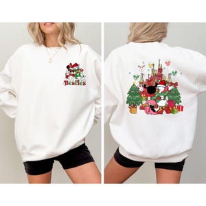 May include: White sweatshirt featuring a Christmas-themed graphic of Mickey and Minnie Mouse, with the text "Besties" on the front. The back of the sweatshirt has a larger design with Mickey, Minnie, and Donald Duck in front of a castle and Christmas trees.