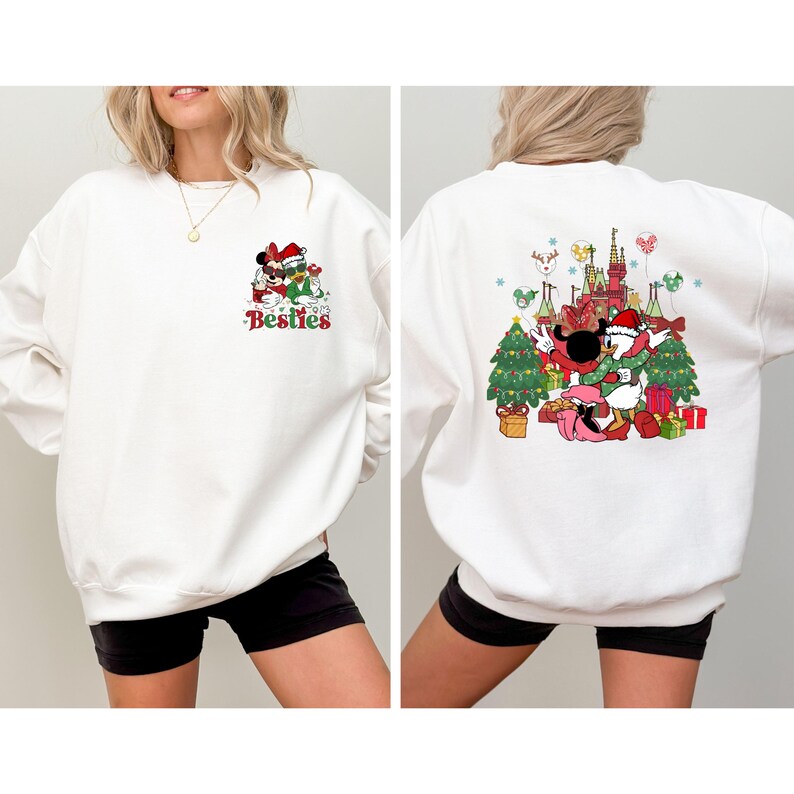 May include: White sweatshirt featuring a Christmas-themed graphic of Mickey and Minnie Mouse, with the text "Besties" on the front. The back of the sweatshirt has a larger design with Mickey, Minnie, and Donald Duck in front of a castle and Christmas trees.