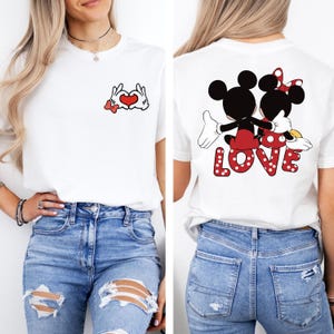 May include: White t-shirt with a red heart and Mickey Mouse hand gestures on the front and Mickey and Minnie Mouse holding hands with the word "LOVE" on the back.