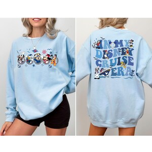 May include: Light blue sweatshirt with a graphic of Disney characters on a cruise ship. The text on the back reads "In My Disney Cruise Era".
