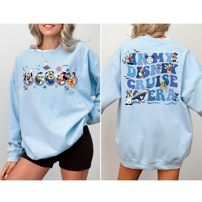 May include: Light blue sweatshirt with a graphic of Disney characters on a cruise ship. The text on the back reads "In My Disney Cruise Era".