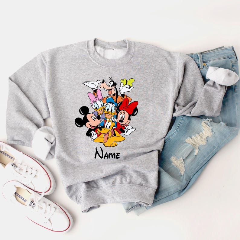 Op de afbeelding: Grijs sweatshirt met een kleurrijke afbeelding van Mickey Mouse, Minnie Mouse, Donald Duck, Goofy en Pluto. De tekst "Name" staat onder de afbeelding.