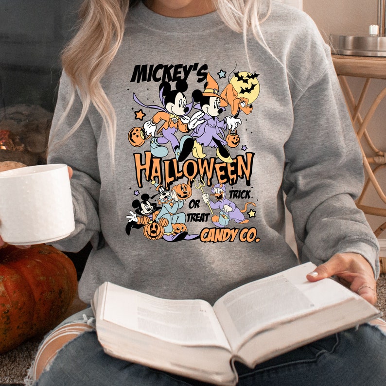 May include: A gray sweatshirt with a Mickey Mouse Halloween design. The design features Mickey and Minnie Mouse dressed in Halloween costumes, along with Pluto and Goofy. The text on the sweatshirt reads "Mickey's Halloween Trick or Treat Candy Co."