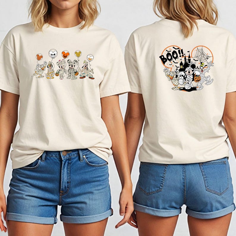 K&ouml;nnte beinhalten: Cremefarbenes T-Shirt mit einem Halloween-Motiv auf der Vorder- und R&uuml;ckseite. Das Frontdesign zeigt Zeichentrickfiguren in Kost&uuml;men mit Luftballons. Das R&uuml;ckendesign sagt "BOO!!" mit einem gruseligen Schloss und Figuren.