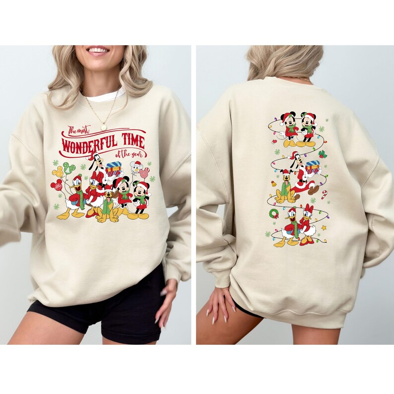 May include: A beige sweatshirt featuring a festive design with Disney characters. The front displays Mickey, Minnie, Donald, and Goofy with the text "The most Wonderful Time of the year". The back has a vertical design of characters with Christmas lights.