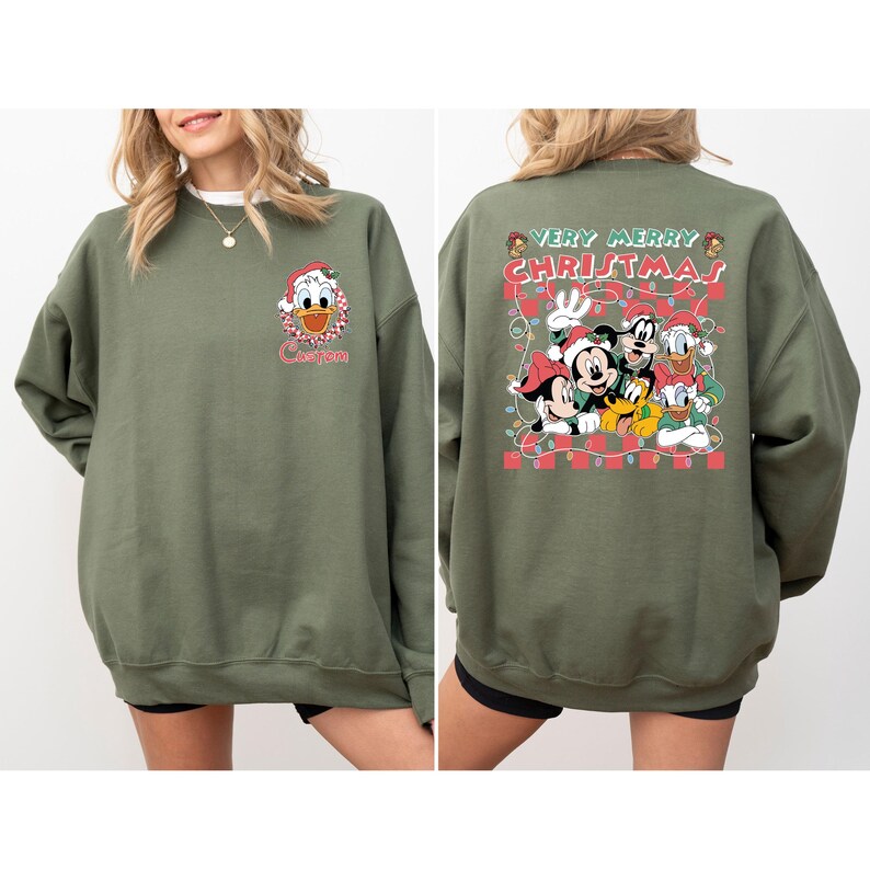 May include: Olive green sweatshirt featuring Donald Duck in a Santa hat with the word "Custom" below. The back of the sweatshirt displays Mickey Mouse, Goofy, Donald Duck, and Pluto with the text "Very Merry Christmas" in a festive design.