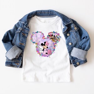 May include: White t-shirt with a pink and purple floral design featuring Mickey Mouse and Minnie Mouse. The design is in the shape of Mickey Mouse's head.