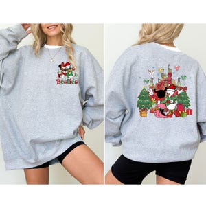 May include: A light gray sweatshirt featuring a colorful graphic of Mickey and Minnie Mouse in Santa hats, with the word "Besties" below. The back of the sweatshirt has a matching graphic with Donald Duck and Daisy Duck, Christmas trees, and a castle.
