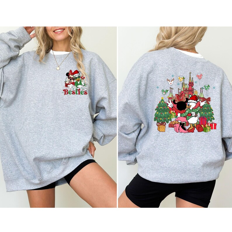 May include: A light gray sweatshirt featuring a colorful graphic of Mickey and Minnie Mouse in Santa hats, with the word "Besties" below. The back of the sweatshirt has a matching graphic with Donald Duck and Daisy Duck, Christmas trees, and a castle.