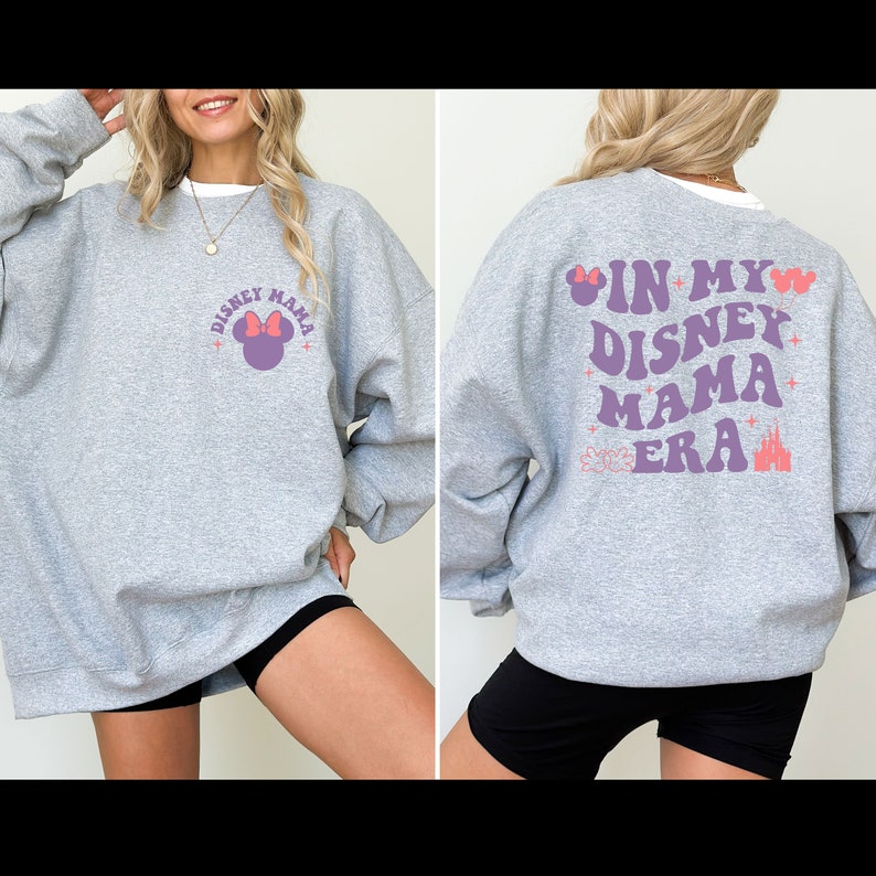 May include: Gray sweatshirt with a purple and pink graphic on the front that says "Disney Mama" with a Mickey Mouse head. The back of the sweatshirt has a purple and pink graphic that says "In My Disney Mama Era" with a Mickey Mouse head and a castle.