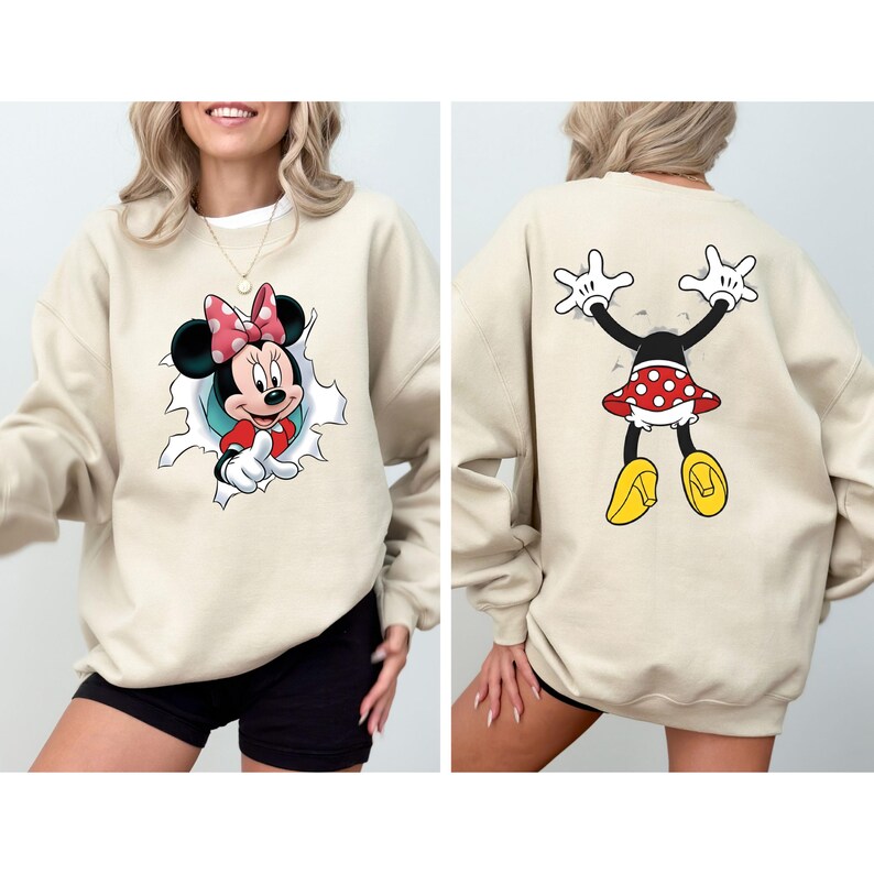 K&ouml;nnte beinhalten: Beiges Sweatshirt mit Minnie Mouse-Motiv. Auf der Vorderseite ist Minnie zu sehen, die aus einem Loch kommt, w&auml;hrend die R&uuml;ckseite sie von hinten zeigt. Minnie tr&auml;gt einen rot-wei&szlig; gepunkteten Rock und eine Schleife mit gelben Schuhen.