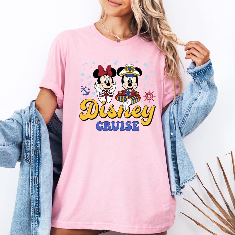 May include: Pink t-shirt with a graphic of Mickey and Minnie Mouse dressed in nautical outfits. The text "Disney Cruise" is printed in yellow on the shirt.