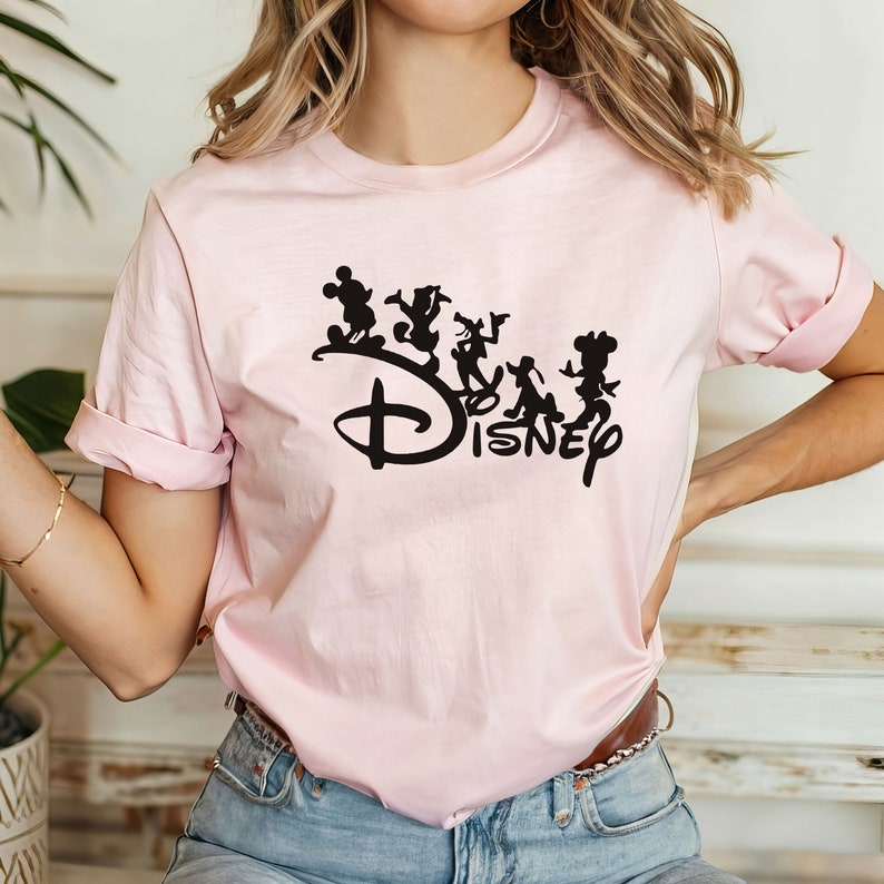 May include: A pink t-shirt with a black silhouette of Mickey Mouse and other Disney characters, along with the word "Disney" in black.