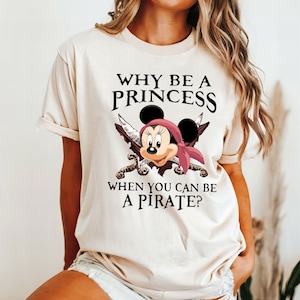 May include: A beige t-shirt with a graphic of Mickey Mouse dressed as a pirate with the text "Why be a princess when you can be a pirate?"