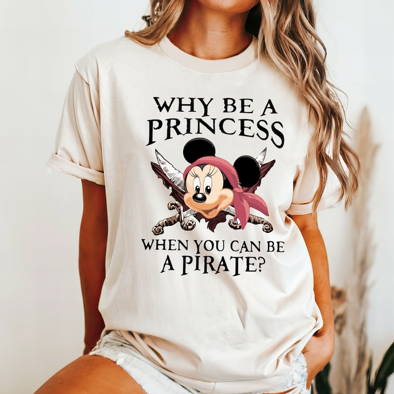 May include: A beige t-shirt with a graphic of Mickey Mouse dressed as a pirate with the text "Why be a princess when you can be a pirate?"
