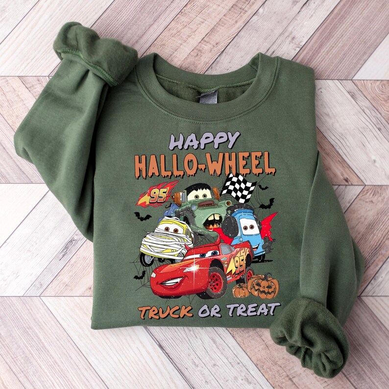 May include: Green sweatshirt with a graphic of cartoon cars from the movie Cars. The text "Happy Hallo-Wheel" is above the cars and "Truck or Treat" is below the cars.