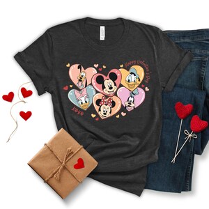 Puede incluir: Una camiseta gris oscuro con un gr&aacute;fico de Mickey Mouse, Minnie Mouse, Donald Duck, Goofy y Pluto en corazones. El texto "Happy Valentine's Day" y "XOXO" tambi&eacute;n est&aacute;n en la camiseta.
