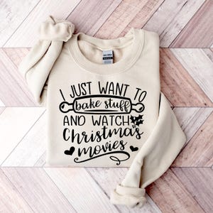 May include: A beige sweatshirt with the text "I just want to bake stuff and watch Christmas movies" in black. A rolling pin graphic is included in the text.