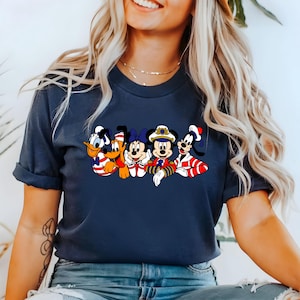 Peut inclure: Un t-shirt bleu marine avec un motif de Mickey Mouse, Minnie Mouse, Donald Duck, Dingo et Pluto habill&eacute;s en marins. Les personnages sourient et saluent.