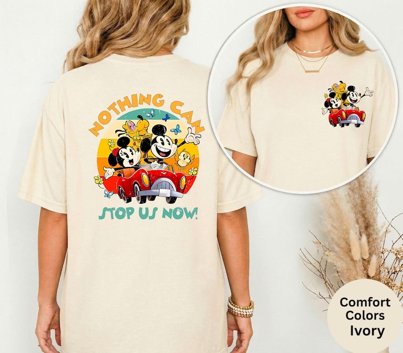 Pode incluir: Camiseta cor marfim com um gr&aacute;fico colorido de Mickey e Minnie Mouse em um carro vermelho, com o texto "NOTHING CAN STOP US NOW!". O design inclui um fundo de p&ocirc;r do sol amarelo, laranja e azul. Uma vers&atilde;o menor do gr&aacute;fico est&aacute; na frente.