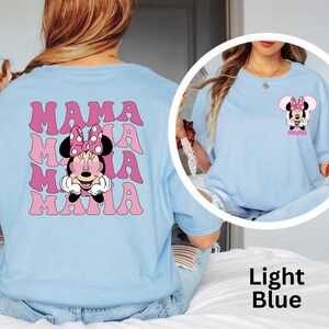 Puede incluir: Camiseta azul claro con un dise&ntilde;o de Minnie Mouse con gafas de sol y la palabra "MAMA" en rosa. La parte trasera de la camiseta tiene un gr&aacute;fico m&aacute;s grande de Minnie Mouse y la palabra "MAMA" repetida.