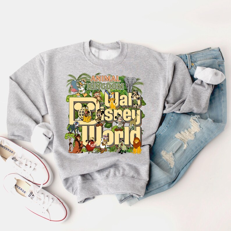 Pu&ograve; includere: Felpa grigia con una stampa grafica del logo di Walt Disney World e personaggi di Animal Kingdom. Il testo recita "Animal Kingdom Walt Disney World".