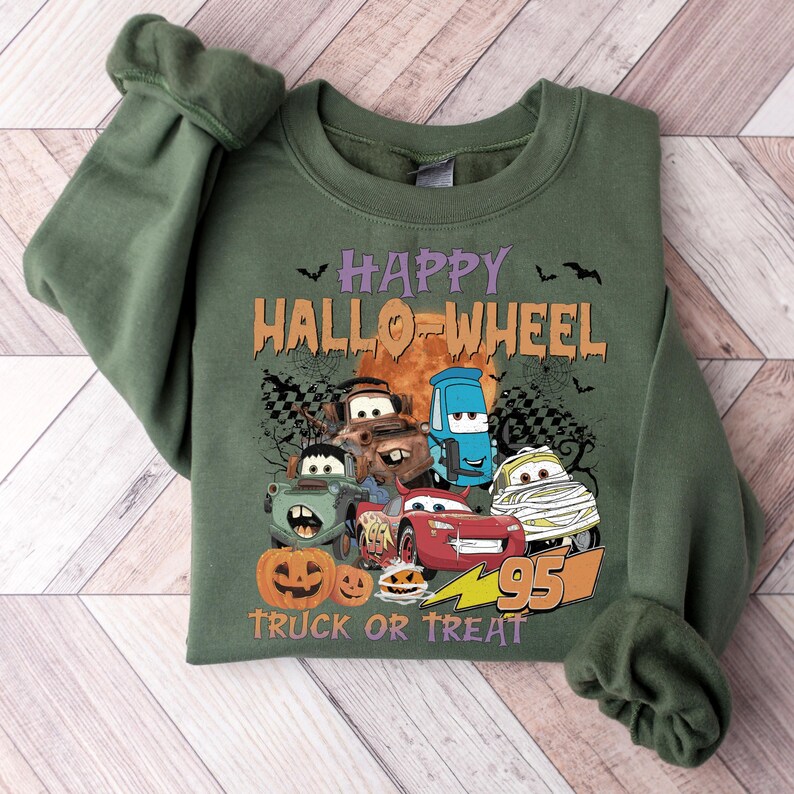 May include: Green sweatshirt with a graphic of Cars characters dressed up for Halloween. The text reads "Happy Hallo-Wheel Truck or Treat" with a lightning bolt and the number 95.