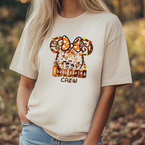 Puede incluir: Camiseta beige con un dise&ntilde;o tem&aacute;tico de Acci&oacute;n de Gracias. El dise&ntilde;o incluye una silueta de Mickey Mouse con un lazo de lunares, hojas de oto&ntilde;o y la frase "Thanksgiving CREW". El gr&aacute;fico es en tonos marrones, naranjas y blancos.