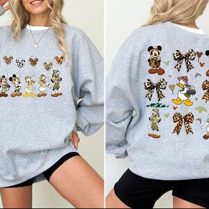 May include: Gray sweatshirt with a print of Disney characters wearing safari outfits and holding balloons. The characters include Mickey Mouse, Minnie Mouse, Donald Duck, Goofy, and Pluto. The print also includes bows and hearts.