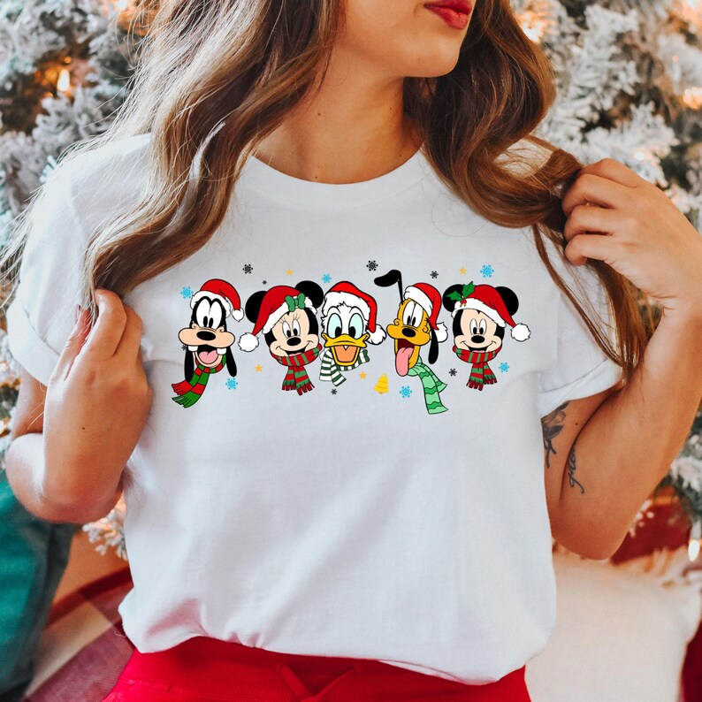 May include: White t-shirt with a Christmas-themed design featuring Mickey Mouse, Minnie Mouse, Donald Duck, Goofy, and Pluto wearing Santa hats and scarves.