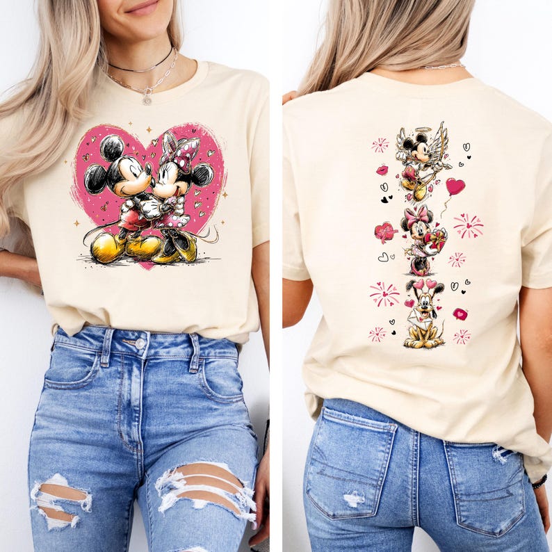 May include: A beige t-shirt featuring a graphic of Mickey and Minnie Mouse embracing within a pink heart. The back of the shirt displays a vertical design with various Disney characters and hearts. The shirt is paired with blue jeans.